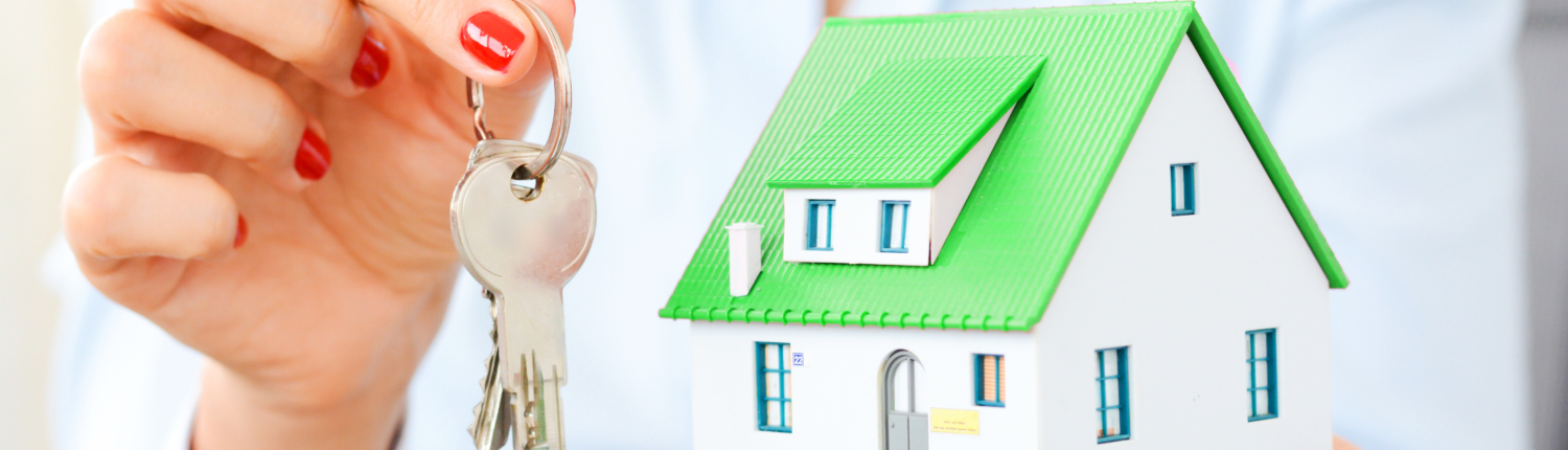 Eine Frau hält das Modell eines Einfamilienhauses mit grünem Dach in einer Hand in der anderen hält sie einen Schlüsselring mit 2 Schlüsseln - Martina Wagner Immobilien