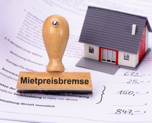 Mietpreisbremse steht auf einem Stempel, der auf einem Mietvertrag steht. Daneben befindet sich noch das Modell eines Hauses - Martina Wagner Immobilien