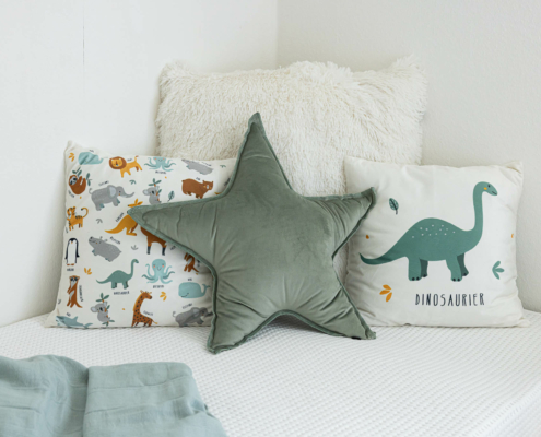 wohnliche Kissen in weiß und salbeitönen und mit Kindermotiven auf einem Bett drapiert - Martina Wagner Immobilien