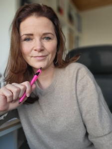 Martina Wagner sitzt am Schreibtisch man sieht einen pinken Kugelschreiber in ihrer Hand