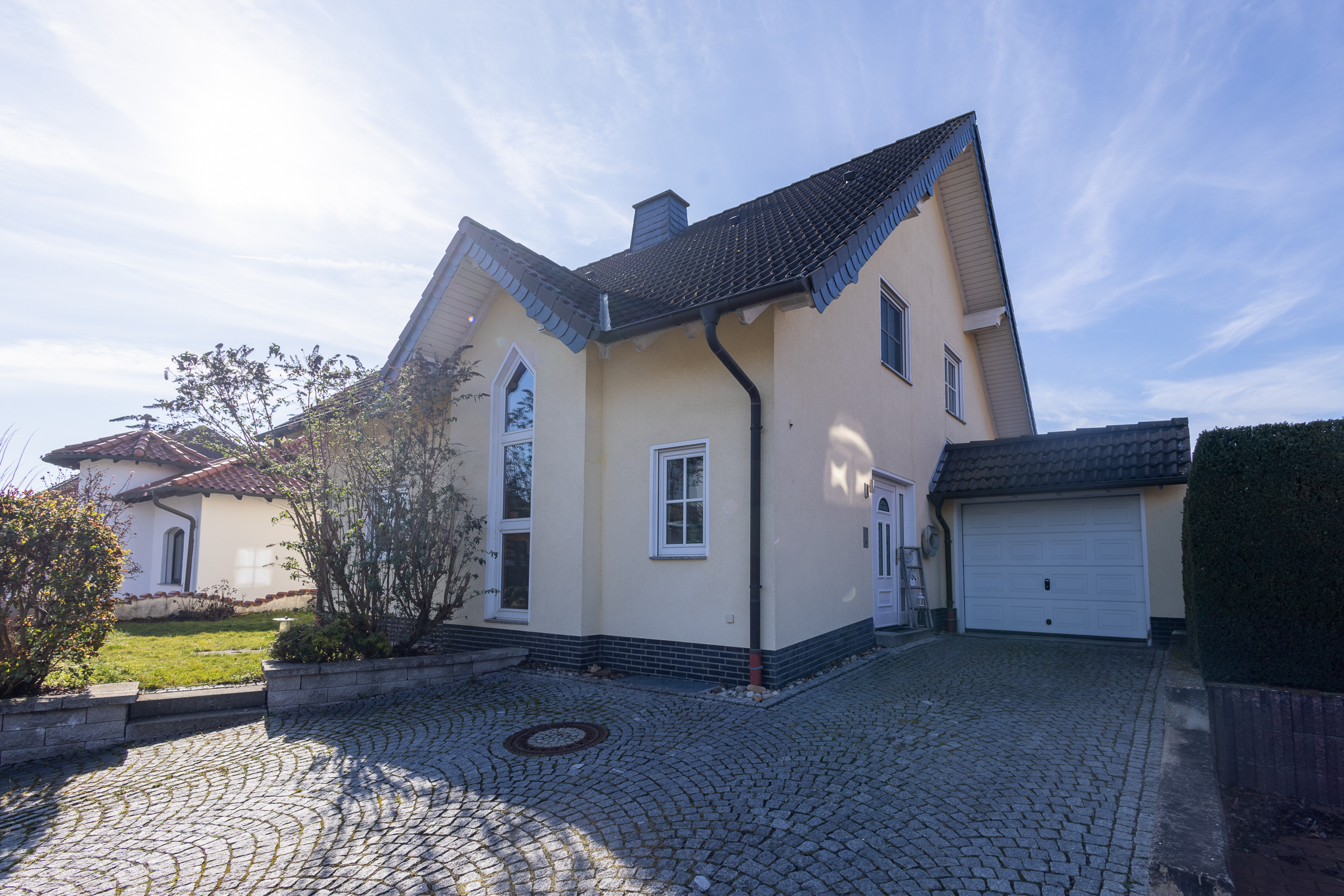 Seitliche Außenansicht der Immobilie in Oberlützingen. Gepflasterte Einfahrt, Garage und Vorgarten sind zu sehen