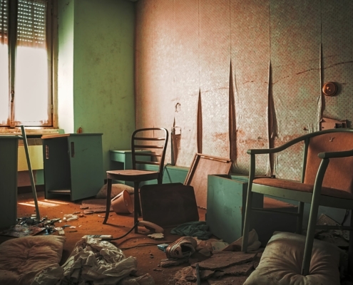 Ausschnitt eines in die Jahre gekommenen Raums mit Resten von Möbeln, Müll und Chaos auf dem Boden, in den Farben grün und orange gehalten