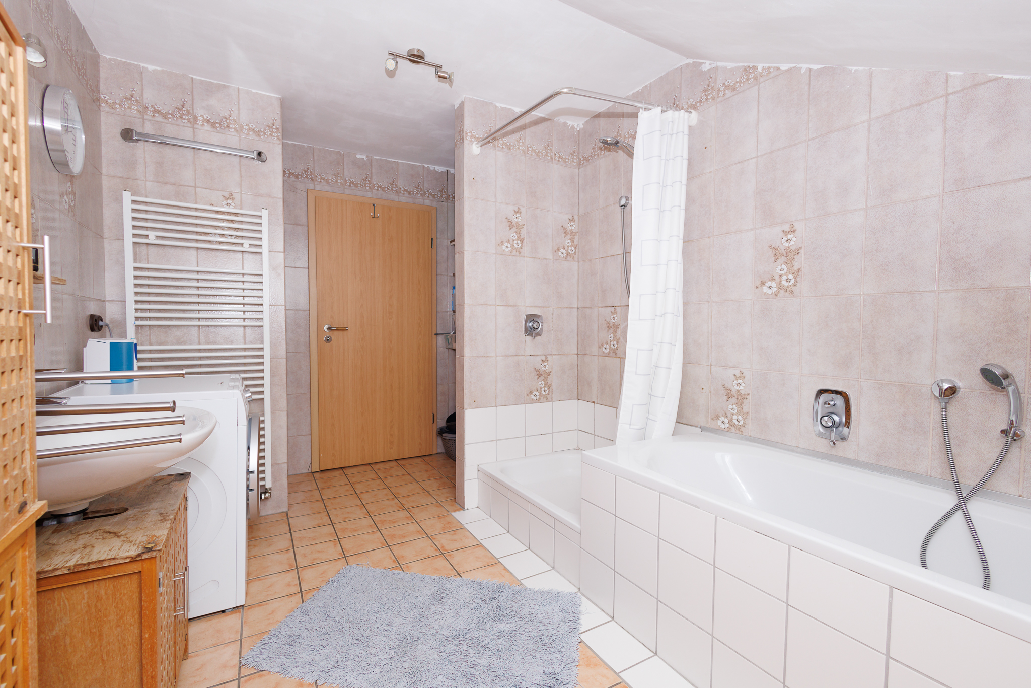 Teilmodernisiertes Bad in Wohnung 1 mit Wanne, Dusche und Waschbecken, hellen Fliesen.