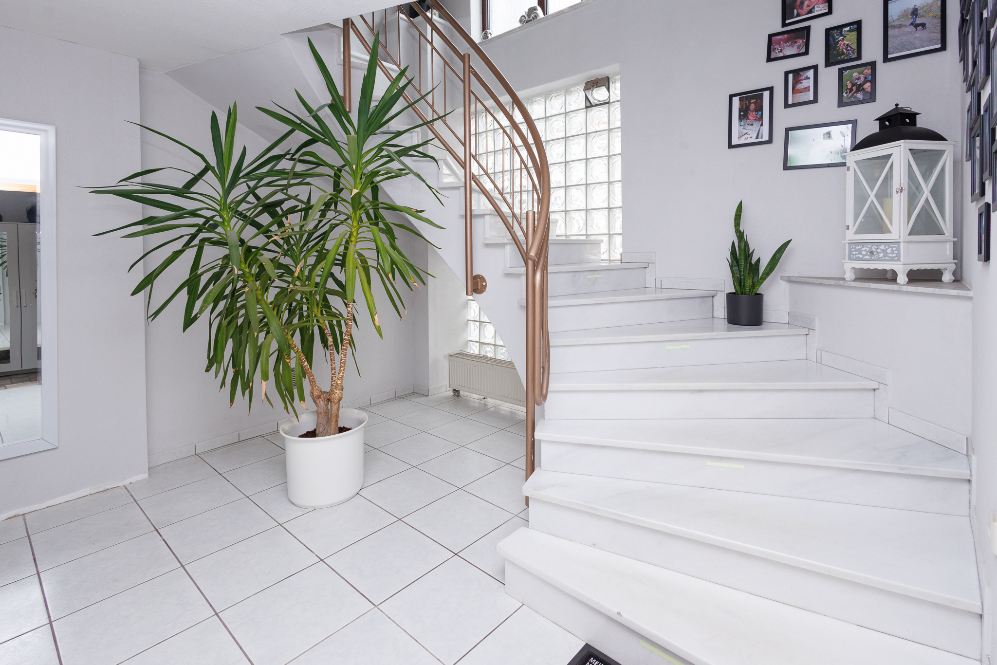 hochwertige weiße Marmortreppe, rechts mit Absatz mit weißer Laterne, mittig große Palme, weißer Fliesenboden, links erkennt man einen Spiegel